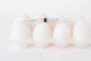 Chicken eggs on a white background on which lies a syringe in which there is a chemical substance, hormones, close-up photo