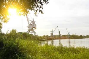Port cranes with a bucket on the river bank, extraction of river sand, the sun photo
