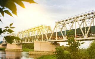 The freight train is moving along the railway bridge across the river photo