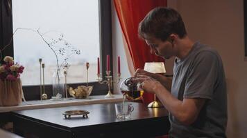 A man at home at a table by the window pours tea video