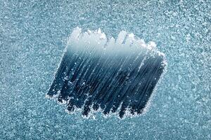 Frosted Window With a Clear Patch Revealing an Icy Blue Background During a Cold Winter Morning photo