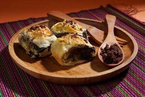 Banana Bolen is made from bananas and pastry dough, filled with chocolate and cheese. It is served on a wooden plate in a selective focus style image. photo