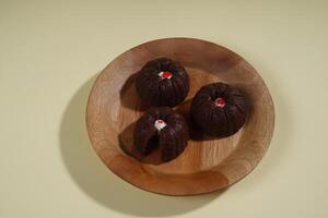 steamed brownie cake with a layer of red and white cream in the middle, served on a wooden plate isolated on yellow background photo