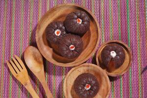 steamed brownie cake with a layer of red and white cream in the middle, served on a wooden plate placed on a rainbow-colored mat photo