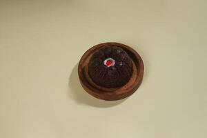 steamed brownie cake with a layer of red and white cream in the middle, served on a wooden plate isolated on yellow background photo