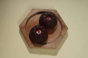 steamed brownie cake with a layer of red and white cream in the middle, served on a wooden plate isolated on yellow background photo