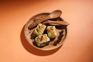 Banana Bolen is made from bananas and pastry dough, filled with chocolate and cheese. It is served on a wooden plate in a selective focus style image. photo