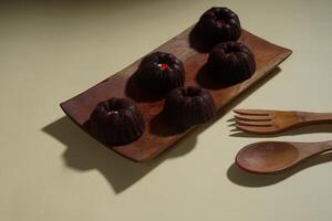 steamed brownie cake with a layer of red and white cream in the middle, served on a wooden plate isolated on yellow background photo