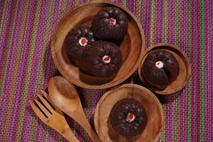 steamed brownie cake with a layer of red and white cream in the middle, served on a wooden plate placed on a rainbow-colored mat photo