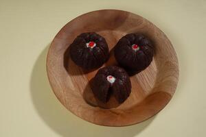 steamed brownie cake with a layer of red and white cream in the middle, served on a wooden plate isolated on yellow background photo