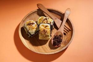 Banana Bolen is made from bananas and pastry dough, filled with chocolate and cheese. It is served on a wooden plate in a selective focus style image. photo