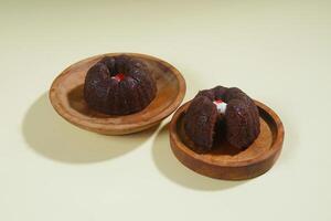 steamed brownie cake with a layer of red and white cream in the middle, served on a wooden plate isolated on yellow background photo