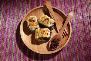 Banana Bolen is made from bananas and pastry dough, filled with chocolate and cheese. It is served on a wooden plate in a selective focus style image. photo