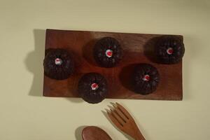 steamed brownie cake with a layer of red and white cream in the middle, served on a wooden plate isolated on yellow background photo
