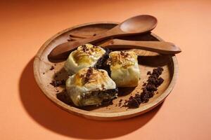 Banana Bolen is made from bananas and pastry dough, filled with chocolate and cheese. It is served on a wooden plate in a selective focus style image. photo