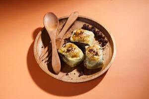 Banana Bolen is made from bananas and pastry dough, filled with chocolate and cheese. It is served on a wooden plate in a selective focus style image. photo