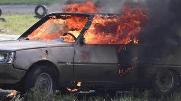 A car burns fiercely in a field, flames engulfing the entire vehicle. Smoke billows into the air as the car is consumed by fire video