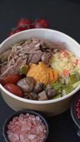 Boiled beef with vegetables, grains, seeds and spices in a ceramic plate on a dark concrete background video