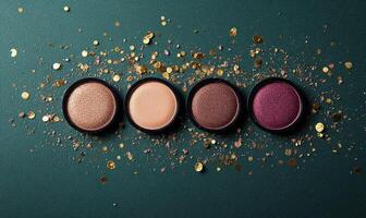 A palette of eyeshadow shades soft rose, muted peach, warm bronze, deep plum, with golden confetti on green background photo