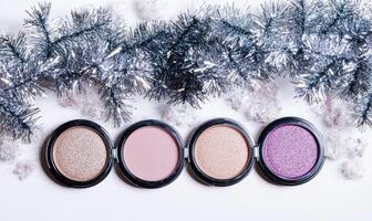 A collection of eyeshadows in soft beige, light blush, peach, and deep violet, decorated with silver tinsel photo