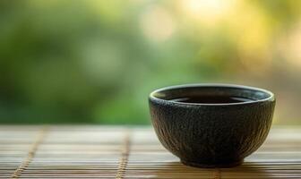 A black ceramic cup with a handle sits on a bamboo mat photo