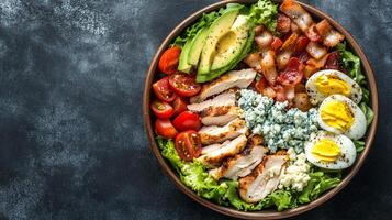 Cobb salad in a round bowl with chicken, bacon, avocado, eggs, tomatoes, and blue cheese crumbles, culinary photography photo