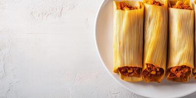 Row of tamales with corn husks partially opened, revealing the filling, on a plain white plate, culinary photography photo