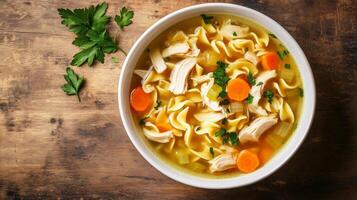 Bowl of chicken noodle soup with floating chicken, noodles, and vegetables, food setting photo