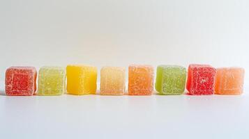 Several fruit chew pieces placed side by side, forming a color gradient on a solid white surface, food photography photo