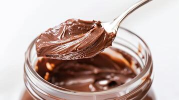 Spoon dipped into a jar of chocolate spread, placed on a plain white background, photorealistic food photo