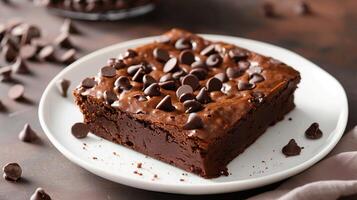Square brownie on a white plate with visible chocolate chips on the top surface, gastronomy photography photo
