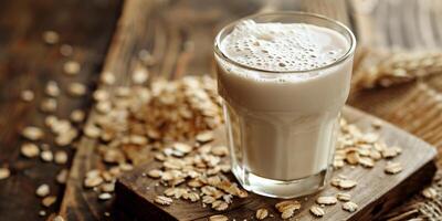 Oat milk in a transparent glass with oats scattered on a wooden surface, meal photography photo