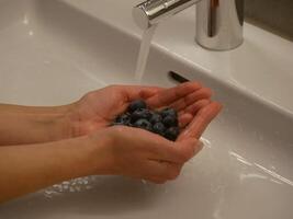 A girl washes blueberries in a sink. Hands under water close-up photo