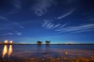 Serenity under the starry night sky, reflecting calm waters and distant trees. A perfect harmony of nature and tranquility photo