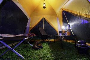 Camping tent, folding bed inside the tent at night in the forest, gas lantern and coffee set, notebook on a camping table, and outdoor ideas. photo