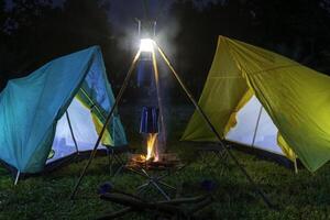 camping tent in the forest with green trees, camping in the forest at night, Small gas lantern on green grass photo