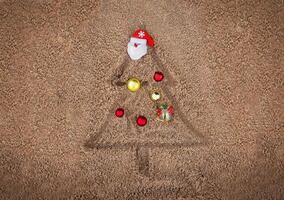 painted christmas tree on the sand on the beach with christmas ornament toy santa photo