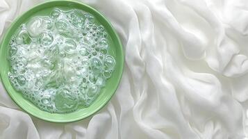 A serene moment with bubbles in a green bowl placed on soft, flowing white fabric during a peaceful afternoon at home photo