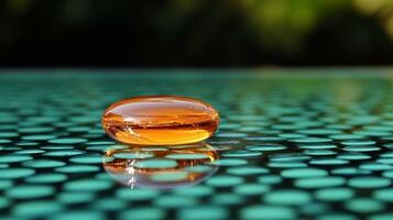 A solitary drop of amber liquid rests on a textured green surface, reflecting warm sunlight photo