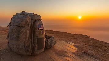 A well-used backpack sits on rocky ground as the sun sets, casting warm light over the landscape photo