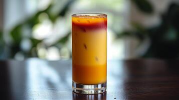 A vibrant orange and red tropical drink sits on a table amidst lush greenery photo