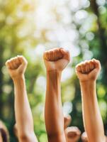 A diverse crowd of individuals raises their fists high in a display of unity, symbolizing solidarity among all attendees during a peaceful protest taking place in a beautifully sunlit park setting photo