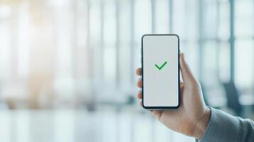 person holding smartphone displaying green check mark, symbolizing approval or success in modern office environment. image conveys sense of achievement and positivity photo