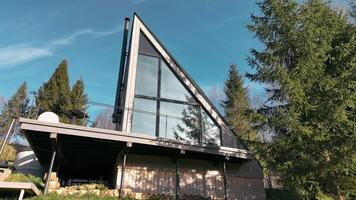 Contemporary A-frame cabin with large glass windows, nestled in a forest setting under a bright blue sky. video