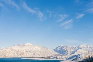 Charvak reservoir with blue water on a clear winter day in Uzbekistan, surrounded by snow-capped mountain peaks of Tien Shan photo