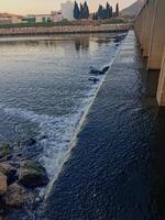 A wide waterfall current under a bridge in Wadi. Close to flowing water, discover complex details photo