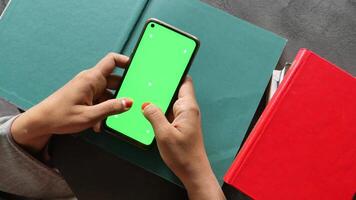 A Person Holding a Smartphone Featuring a Green Screen While Surrounded by Books video