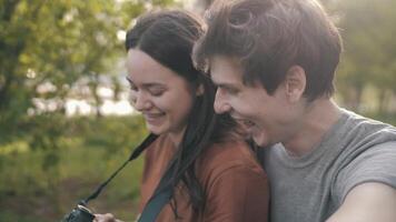 a girl and a guy sit on the grass and look at the photos on the camera video