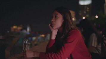 Nighttime Contemplation. A woman sits alone, lost in thought, on a rooftop bar, with the city lights twinkling in the background. video