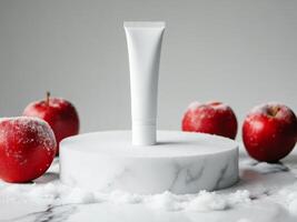 White cosmetics cream tube on white podium standing on marble table. Snow and red apples on background. Minimalistic photo style
